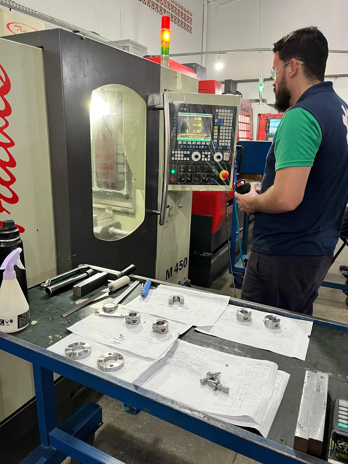Operador da LE Usinagem no painel do centro de usinagem CNC, com a programação da peça na tela