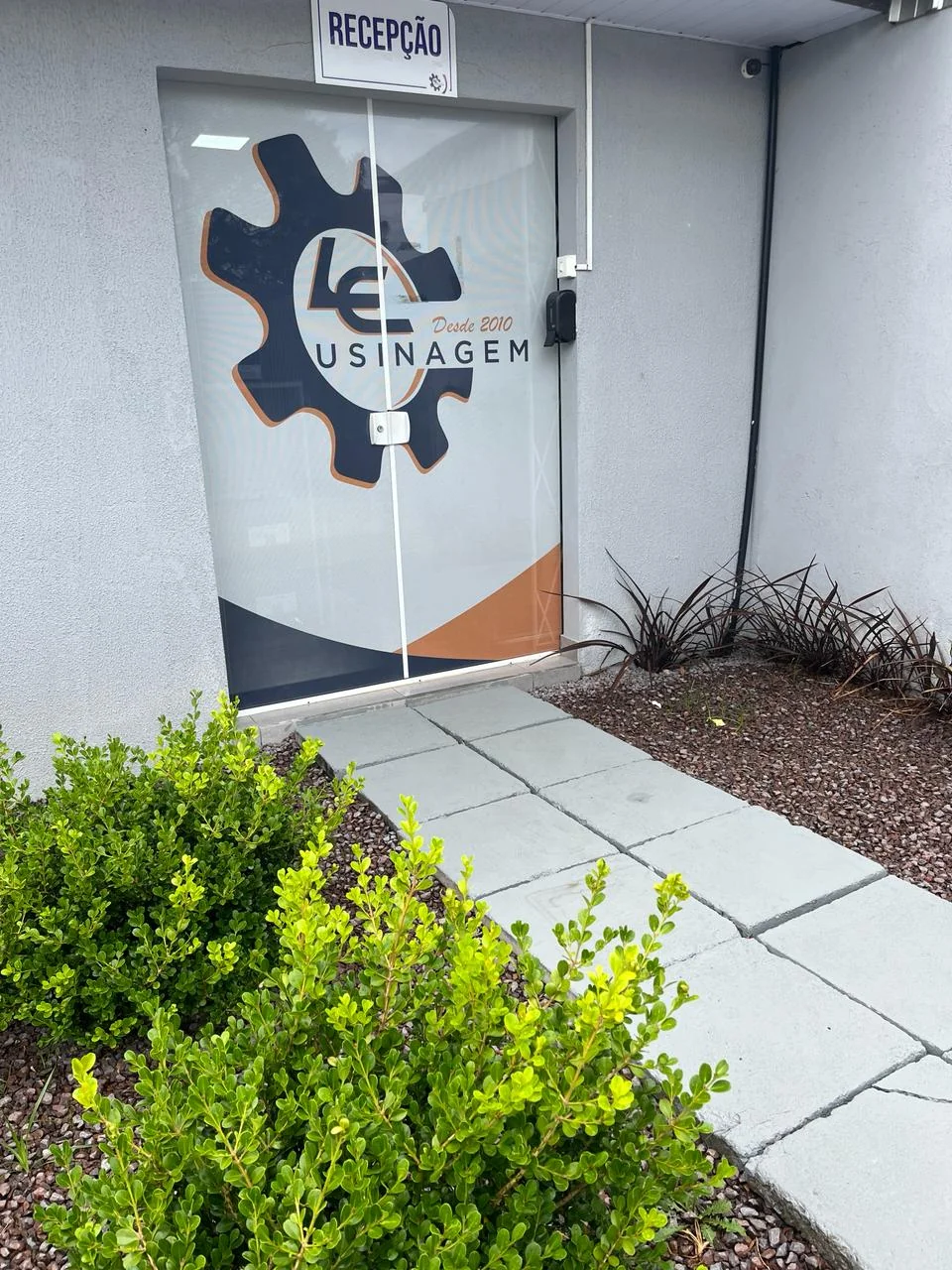 Porta de vidro da recepção da LE Usinagem com adesivo do logotipo, na Rua Aracaju, Costeira, São José dos Pinhais